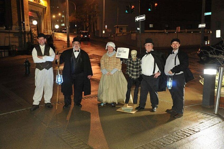 A group of people in period costumes standing on a street at night. 2