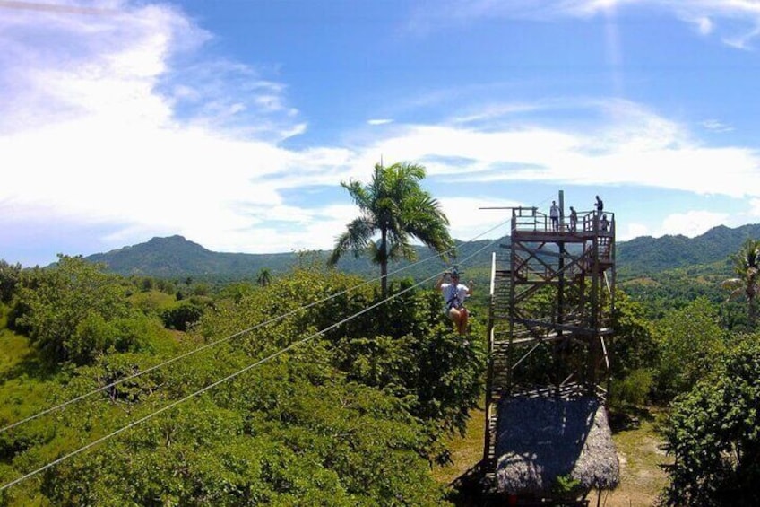 Una torre de observación de madera con un puente colgante, rodeada de exuberante vegetación y colinas al fondo. 1