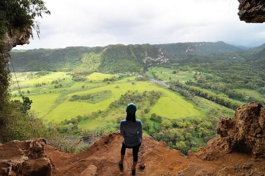 A person standing on a cliff overlooking a green valley with a river. 2
