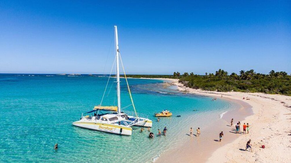 A beach with clear turquoise water, a sailboat, and people enjoying the shore. 2