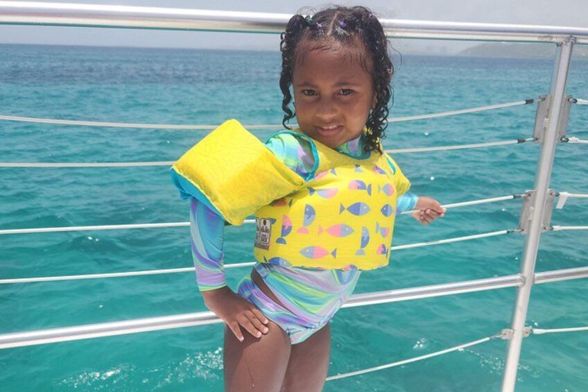 A child on a boat wearing a yellow life jacket with fish patterns. 2