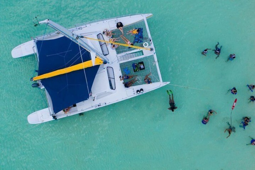 Une vue aérienne d’un petit bateau avec des personnes à bord et de plusieurs personnes qui nagent dans l’eau à proximité. 1
