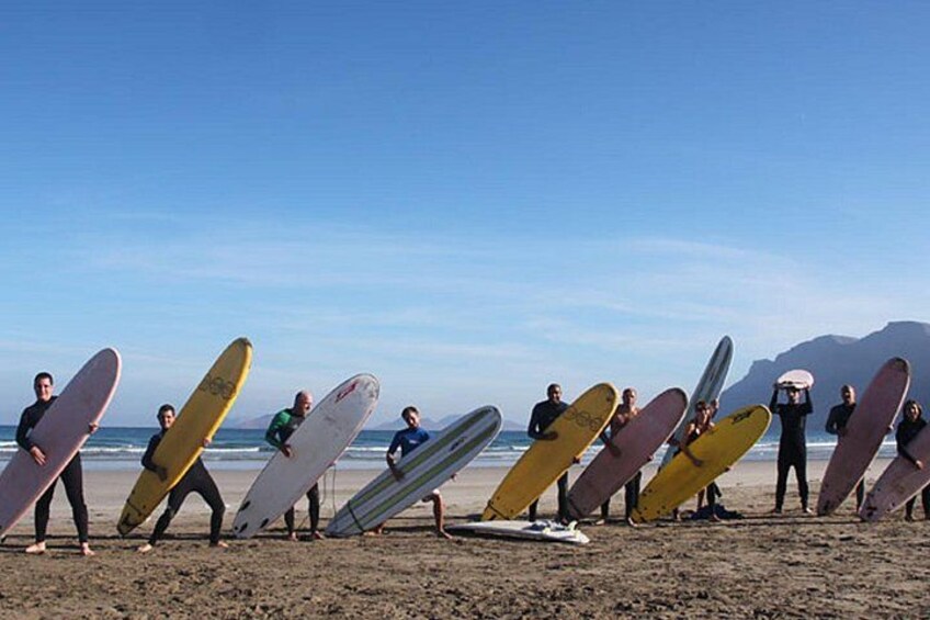 Un grupo de surfistas sosteniendo tablas de surf en una playa con cielos despejados y montañas a lo lejos. 5