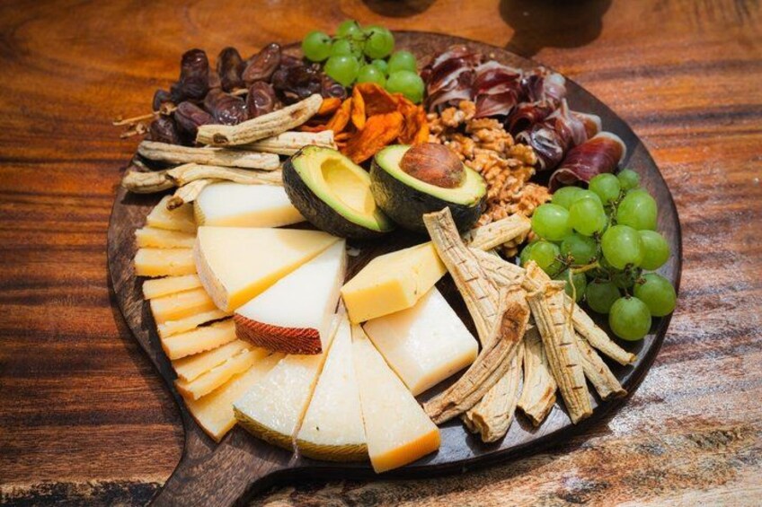 A wooden board with various cheeses, grapes, nuts, and dried fruits. 3