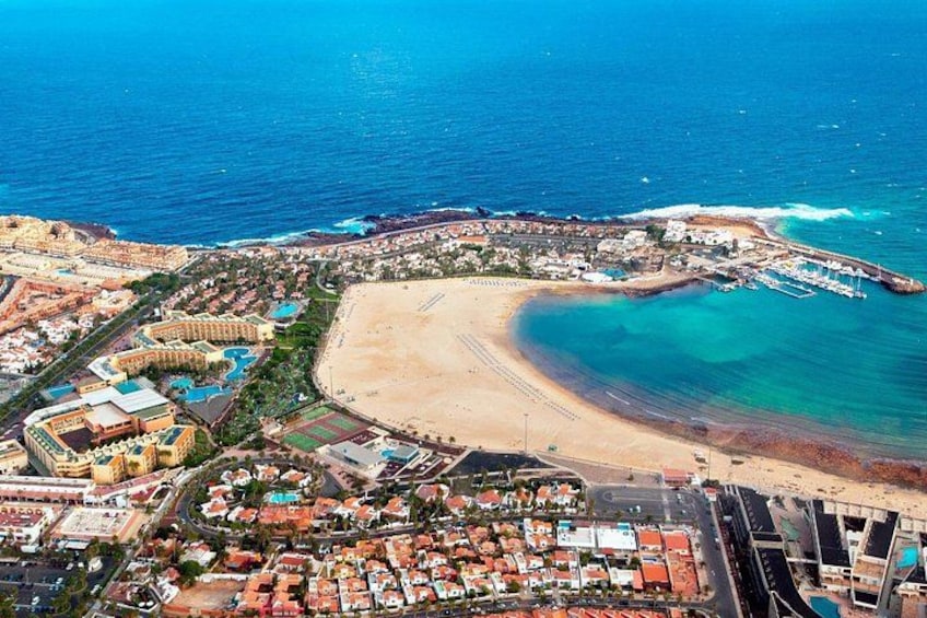 An aerial view of a coastal resort with a sandy beach, a marina, and a large hotel complex. 2