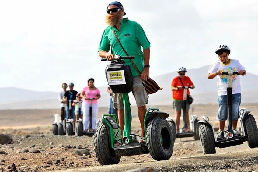 Una persona in sella a un Segway su una strada sterrata, con un paesaggio desertico sullo sfondo. 1