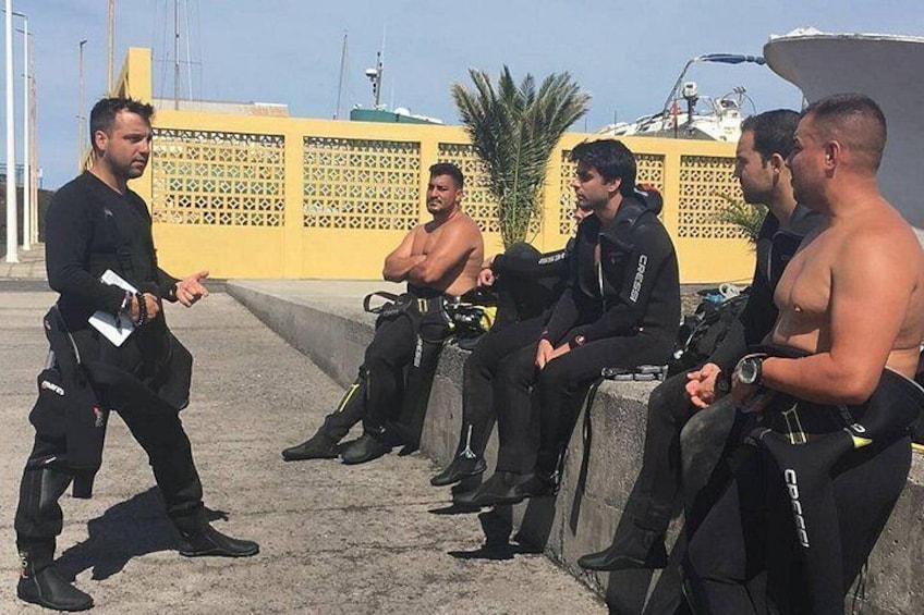 A group of divers in black wetsuits and scuba gear, sitting on a concrete ledge. 4