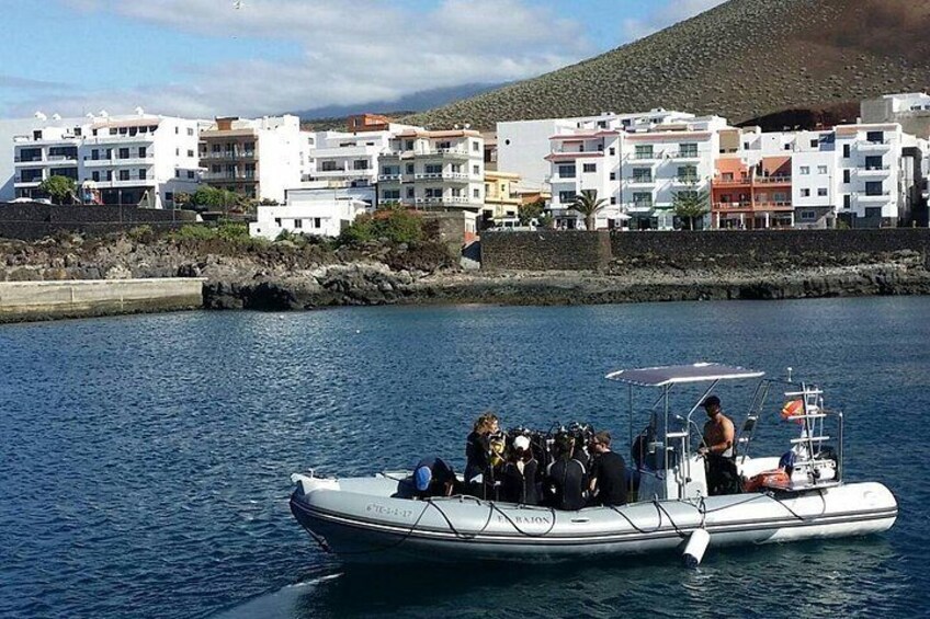 A small boat with people on it, a rocky shoreline, and buildings in the background. 3
