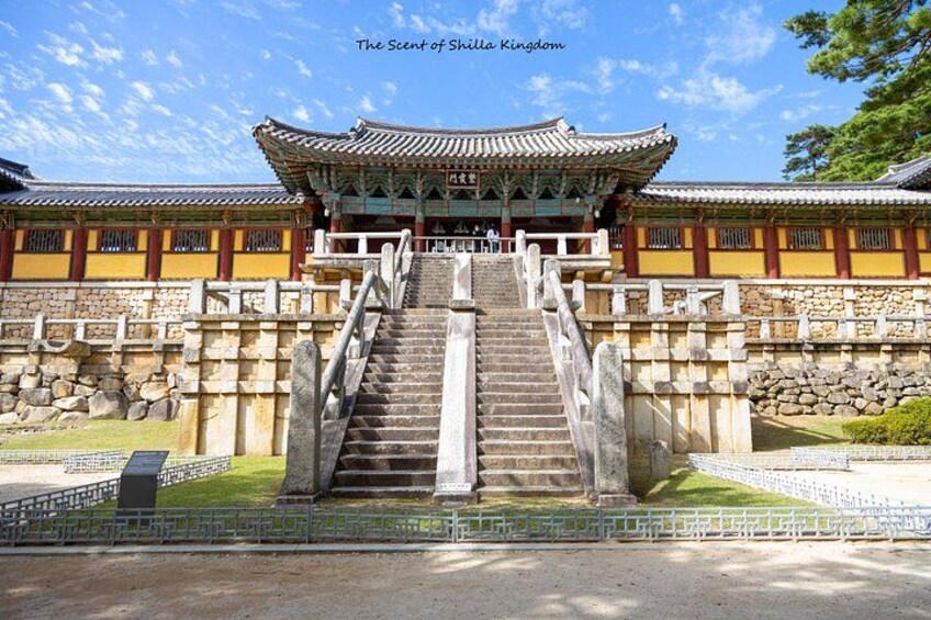 A traditional Korean palace with a large staircase leading to a main gate, surrounded by stone walls and a well-maintained garden. 3