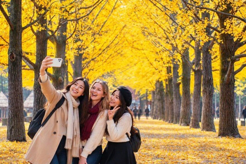 En grupp människor som tar en selfie i en park med gula träd. 1