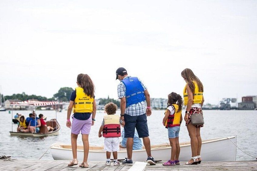 A group of people on a dock by a body of water, some wearing life jackets. 2