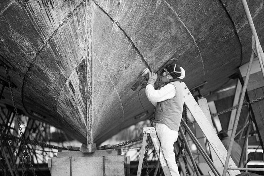 A person working on a large, curved metal structure, possibly a ship or boat, with a ladder and chains visible. 4