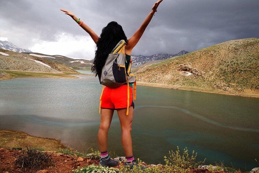 Una persona de pie junto a un lago, con los brazos levantados, usando shorts rojos y una mochila. 2