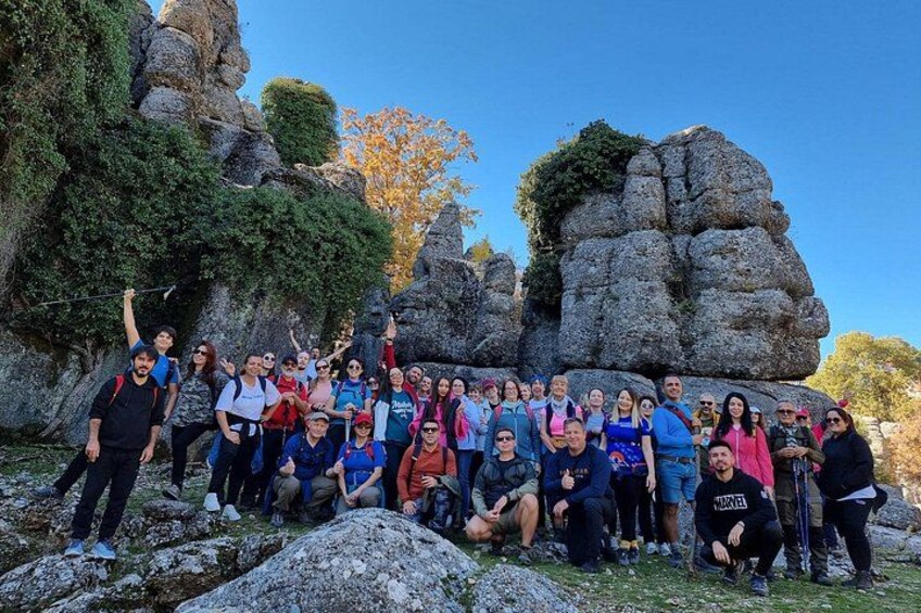 Un grupo de personas posando frente a formaciones rocosas con árboles al fondo. 5