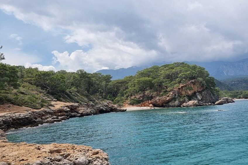 A coastal landscape with rocky shores, a sandy beach, and a forested hill. 4