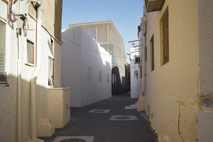 A narrow alleyway with white buildings, a tiled floor, and a clear sky. 1