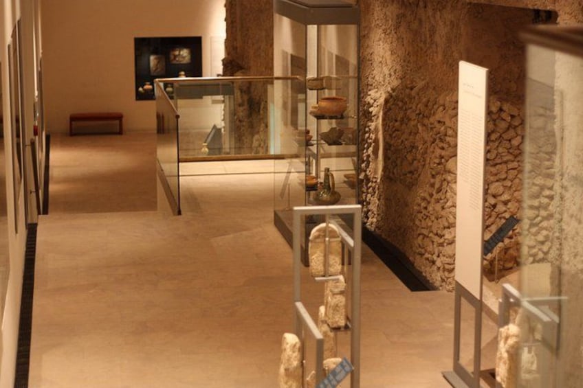 Una exhibición de museo en interior con paredes de piedra, vitrinas de vidrio y artefactos. 4