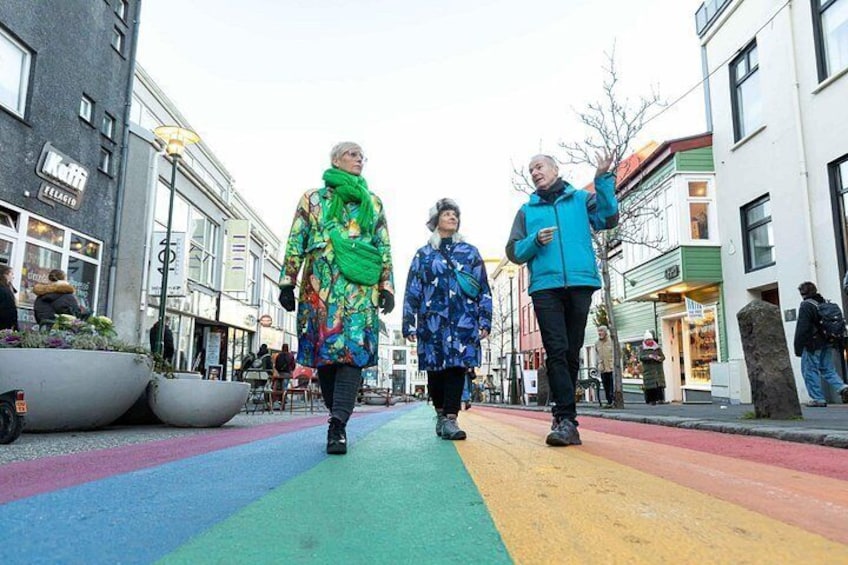 A pedestrian crossing with colorful stripes, buildings on either side, and people walking. 3