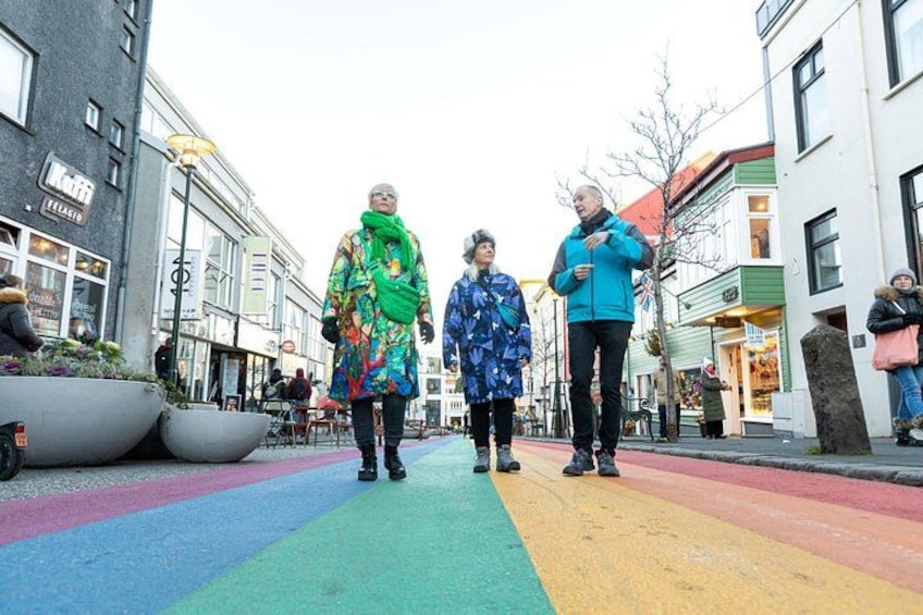 Un attraversamento pedonale con strisce colorate, edifici ai lati e persone che camminano. 2