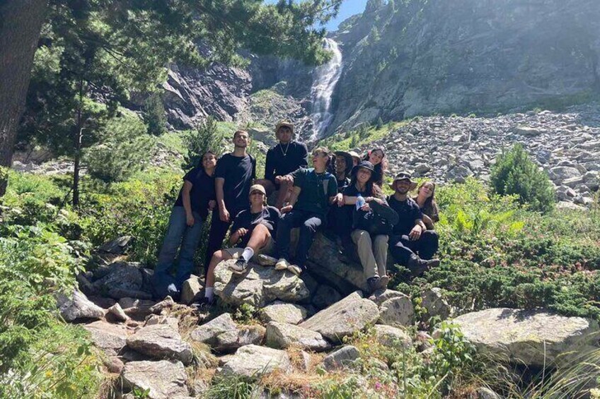 A group of people sitting on rocks near a waterfall in a forested area. 3