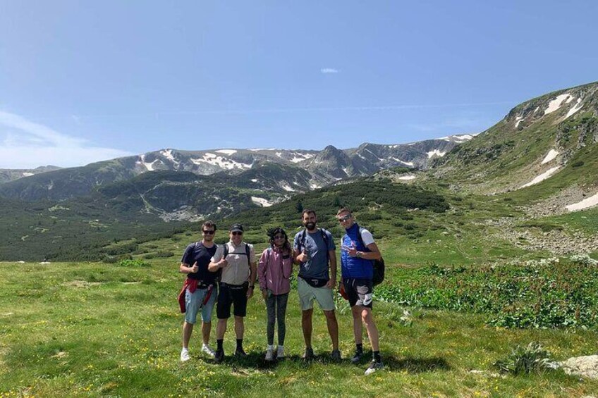 A group of hikers on a grassy mountain trail with snow-capped peaks in the background. 4