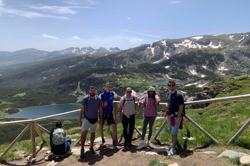 A group of hikers on a mountain trail with a lake and snow-capped peaks in the background. 5