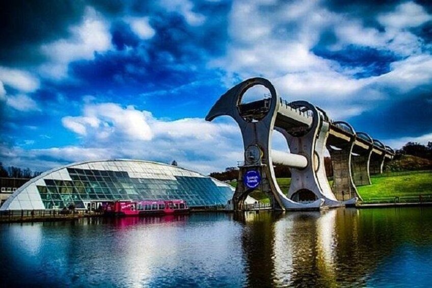 Un bâtiment moderne à la façade vitrée, un pont au design original et un train circulant sur des voies ferrées. 3