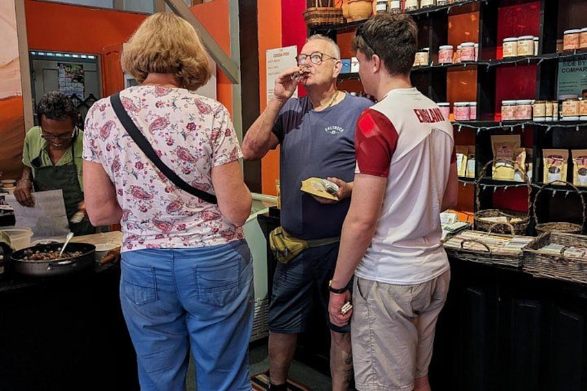 People in a store with shelves of jars and a counter with food items. 2