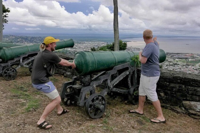 Two people interacting with a cannon on a historical site with a coastal view. 5