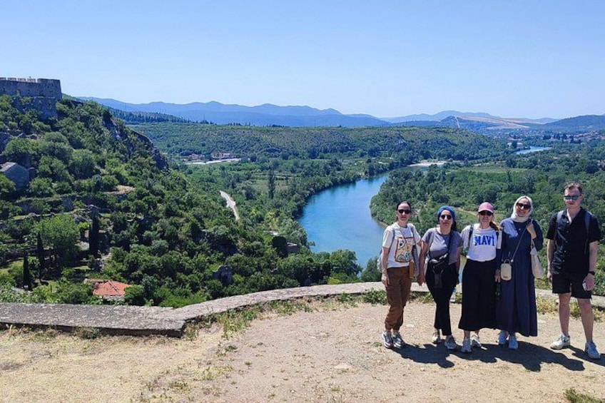 A group of people standing on a hill overlooking a river and a castle. 2