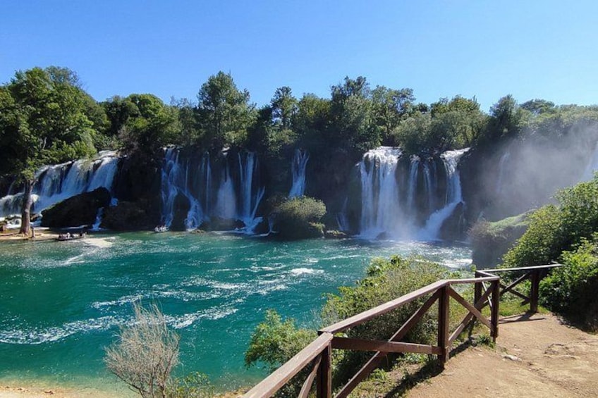 A multi-tiered waterfall, clear turquoise water, and a wooden viewing platform. 2