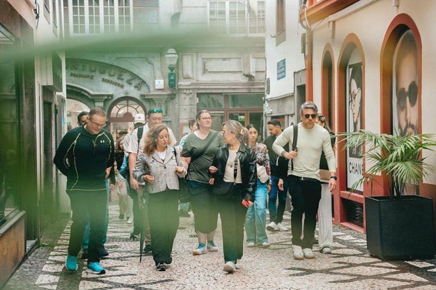 Un groupe de personnes se promène dans une ruelle pavée bordée de bâtiments historiques et d’arcades. 1