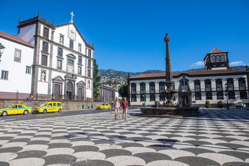 A plaza with patterned pavement, a fountain, and historic buildings. 5