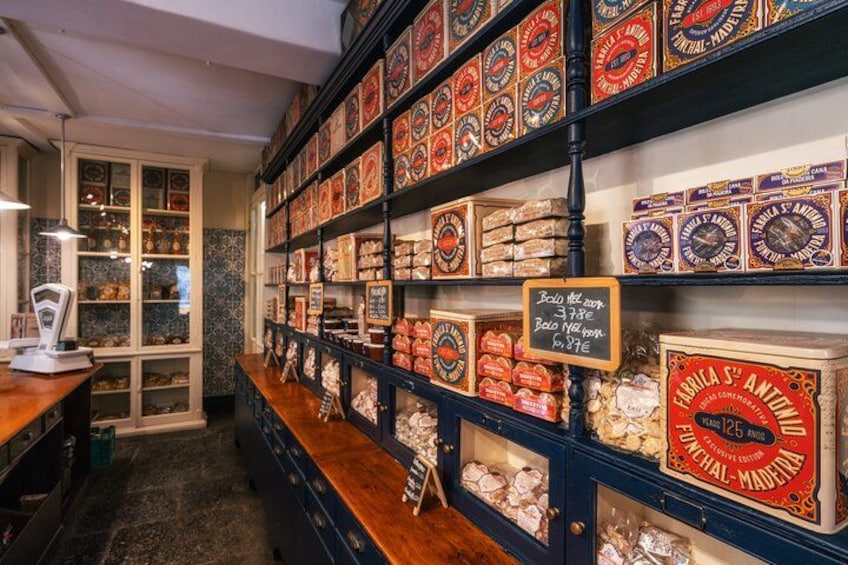A shop with shelves of various packaged goods, a chalkboard with prices, and a wooden counter. 3