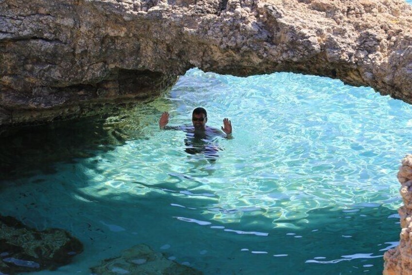 Una persona nadando en una piscina azul cristalina bajo un arco rocoso. 5