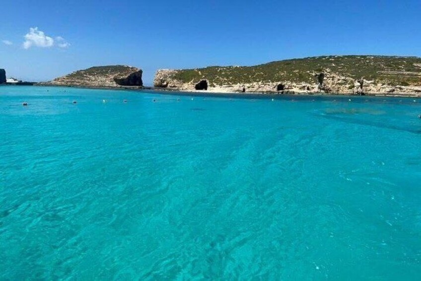 Un mar turquesa cristalino, costa rocosa y la entrada a una pequeña cueva. 2