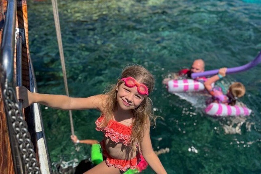 Een persoon in een rood badpak op een boot, met helder water op de achtergrond. 4
