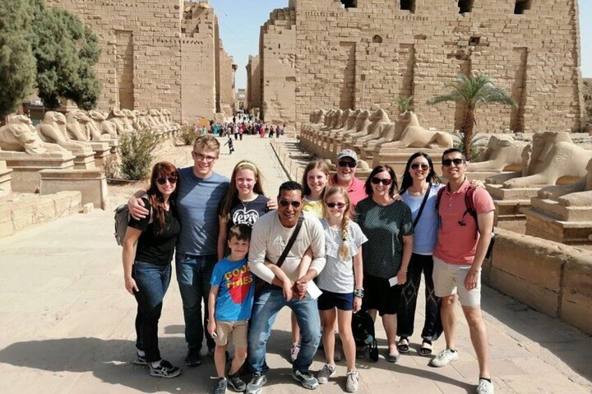 Un groupe de personnes posant devant des ruines de l’Égypte ancienne, avec de grandes structures et statues en pierre. 4