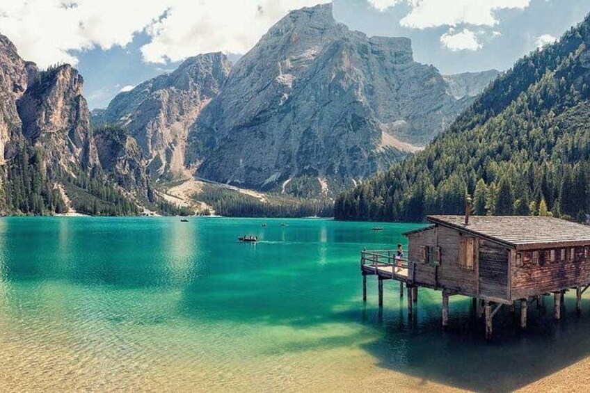 A wooden house on stilts by a turquoise lake with mountains in the background. 3