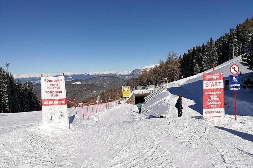 A ski slope with signs indicating a start point and a run named 'RODELBAHN'. 4