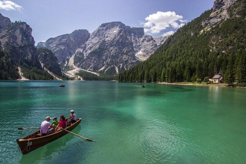 A calm lake surrounded by mountains, a wooden boat with people rowing, and a small house on the shore. 5