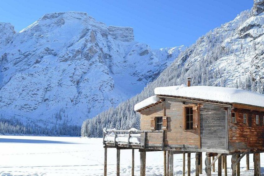 A wooden cabin on stilts in a snowy landscape with mountains in the background. 2