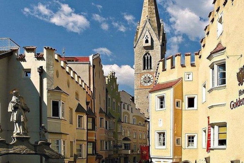 Een straat met historische gebouwen, een kerktoren en een standbeeld. 1