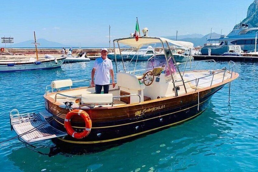 Een houten boot met de naam 'McCallister NL-01' ligt aangemeerd in een jachthaven, met andere boten en een bergachtig landschap op de achtergrond. 4