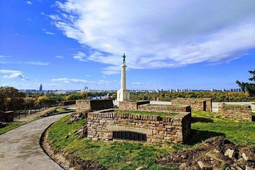 A historical monument with a tall column, surrounded by brick walls and grassy areas. 2