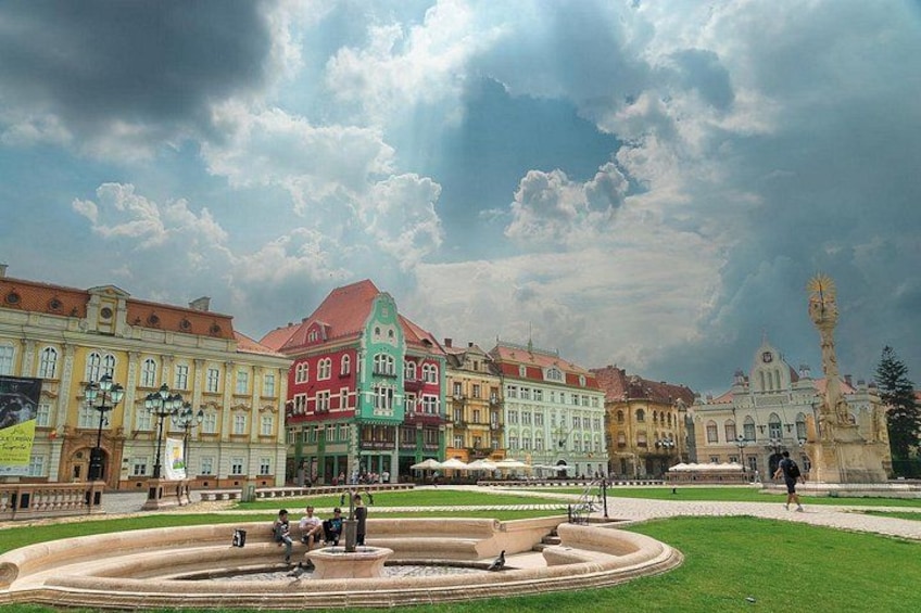 Une place historique bordée de bâtiments aux couleurs vives, avec une fontaine et un beffroi. 2