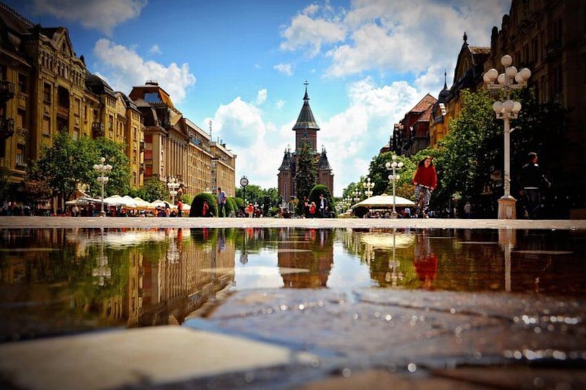 Une place de ville avec une vaste étendue d’eau aux reflets changeants, des b âtiments historiques et un clocher d’église imposant. 1