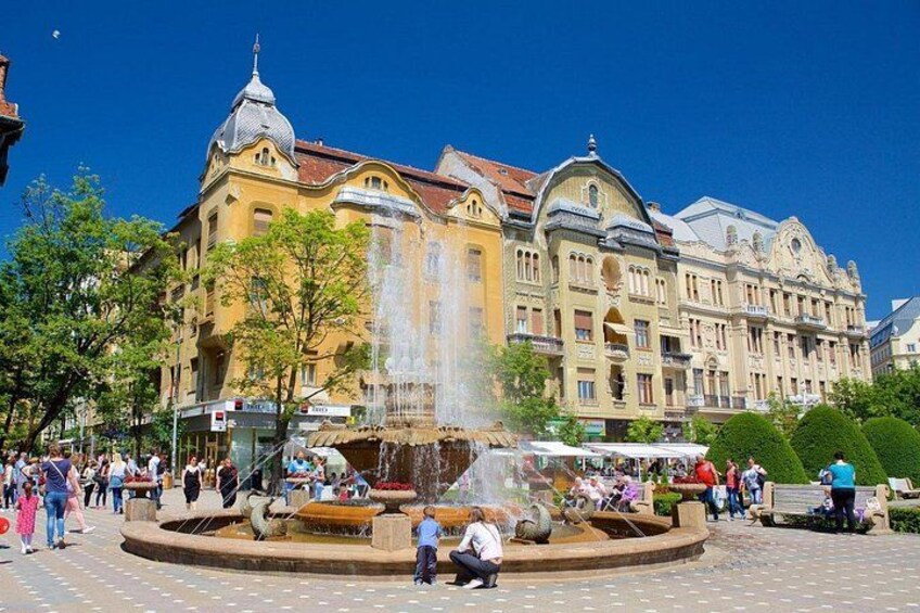 Une place publique avec une fontaine, des bâtiments historiques et des passants. 4
