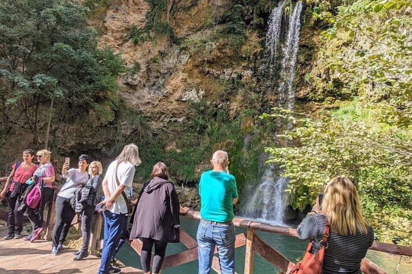 A group of people observing a waterfall and a water feature in a natural setting. 2