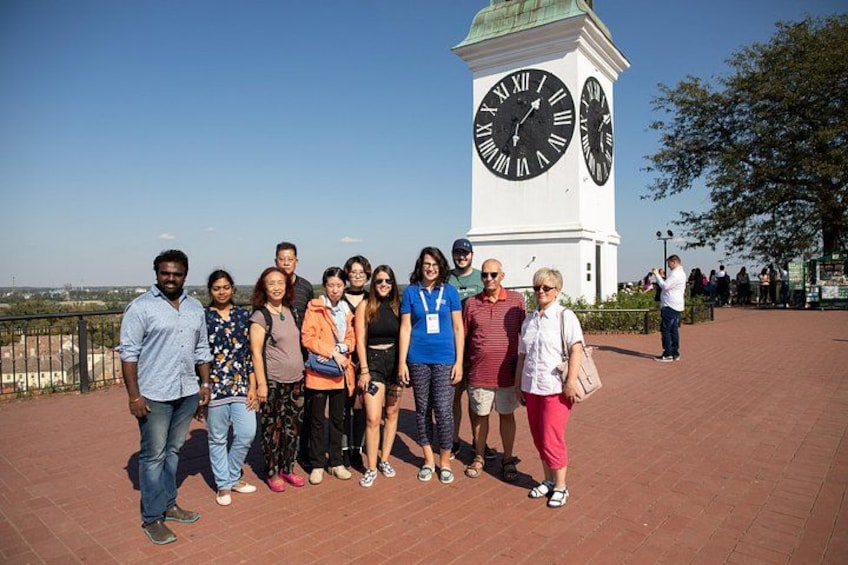 A group of people standing in front of a clock tower with Roman numerals on its face. 2